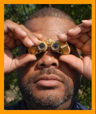 Black man looking through golden binoculars. www.miniaturebinoculars.com